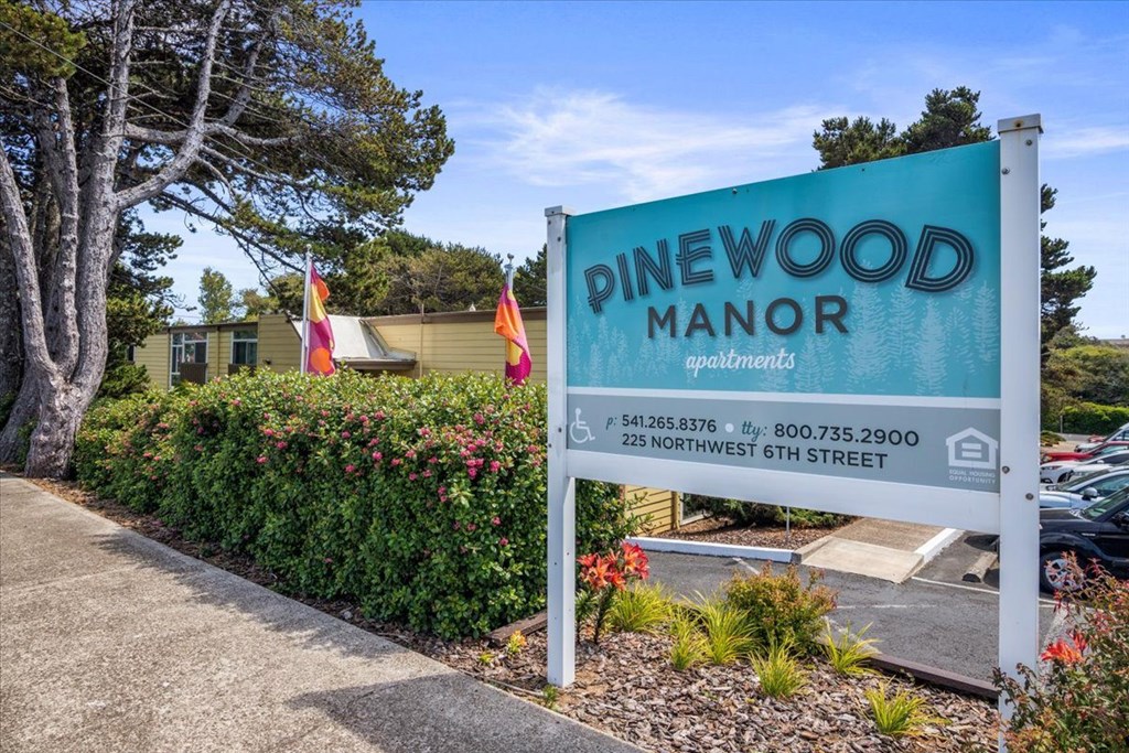 A sign for Pinewood Manor apartments stands in front of a building.