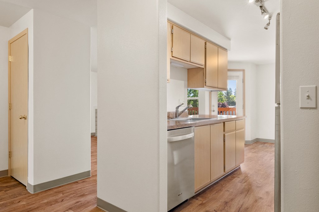 a kitchen with wooden floors and white walls and a stainless steel dishwasher
