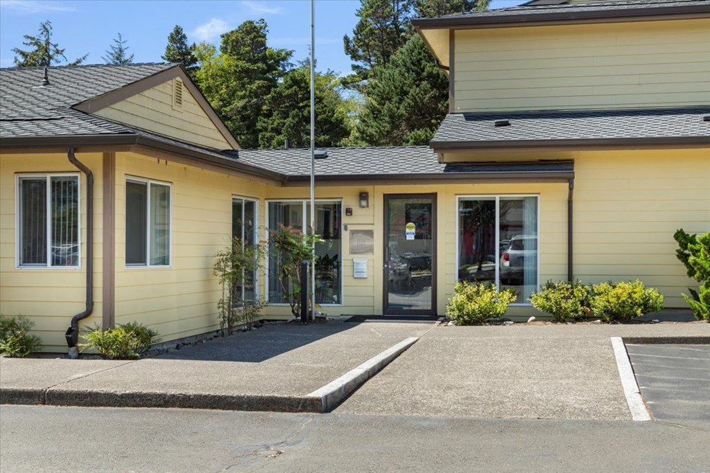A yellow house with a black roof and a grey driveway.