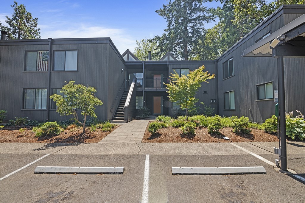 A parking lot in front of a grey building with a flag on the building.