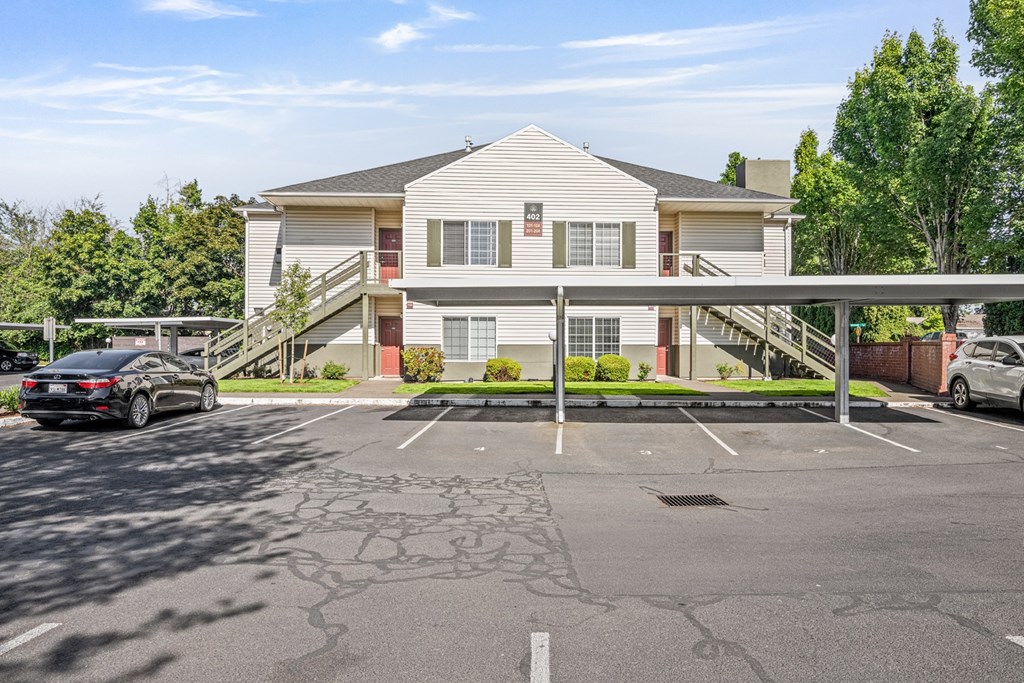 A car is parked in a parking lot in front of a two-story building.