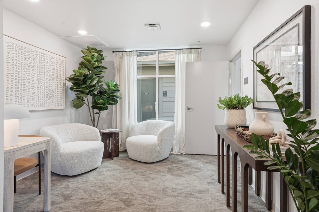 A well-lit, modern living room with a grey carpet, a white sofa, a white armchair, a wooden table, and a potted plant.