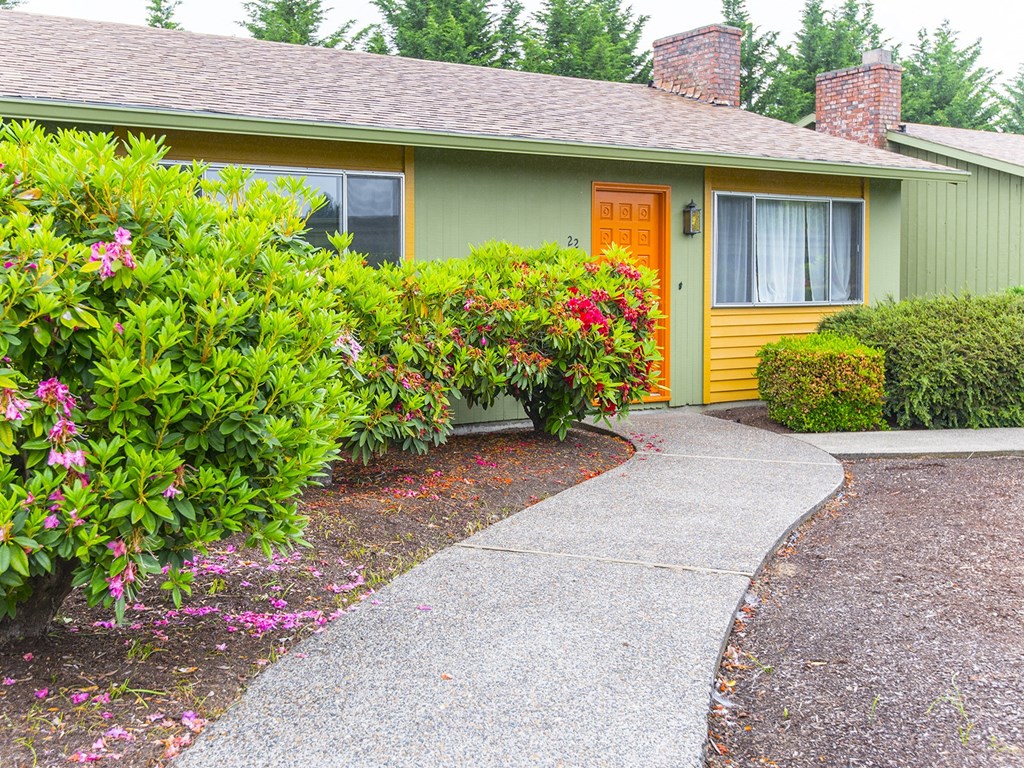 a sidewalk in front of a green house with a orange door