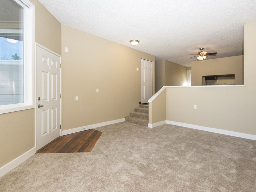 an empty living room with carpet and a door to a staircase