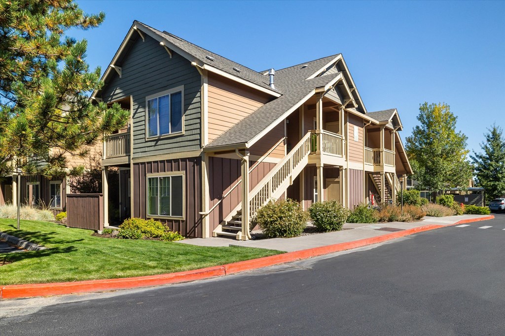 an apartment building with a black asphalt road in front of it and trees in the background