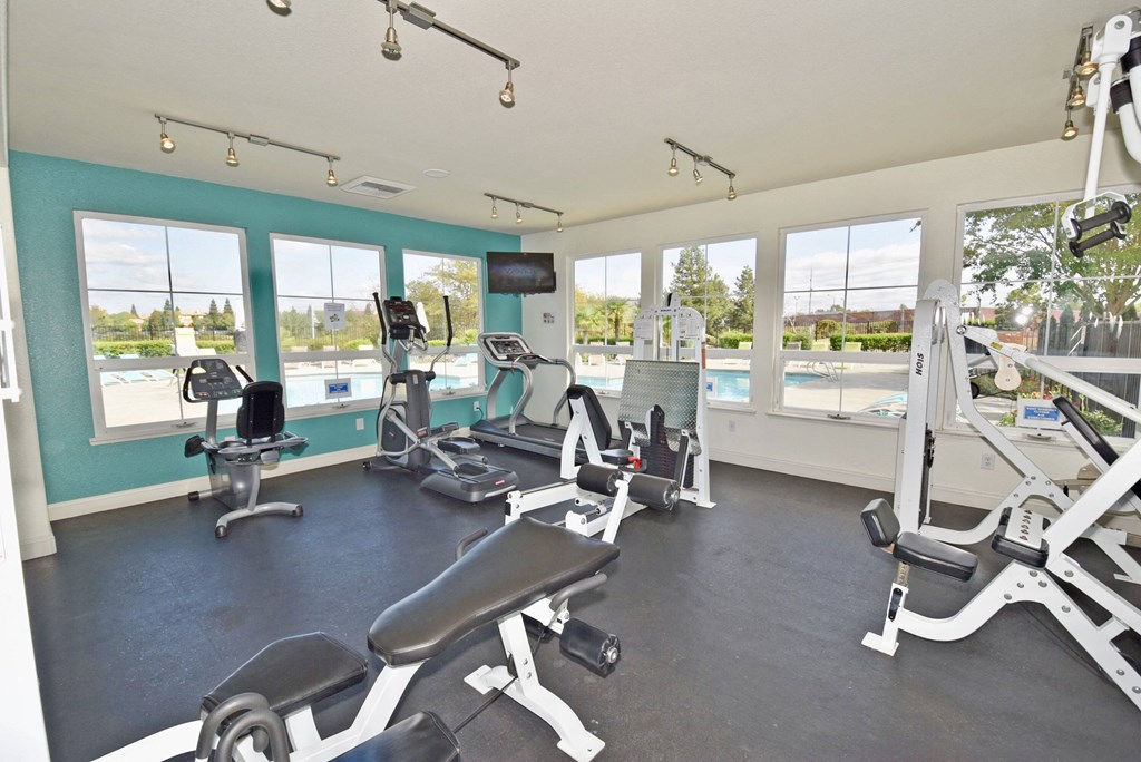 a gym with cardio equipment and windows overlooking a pool