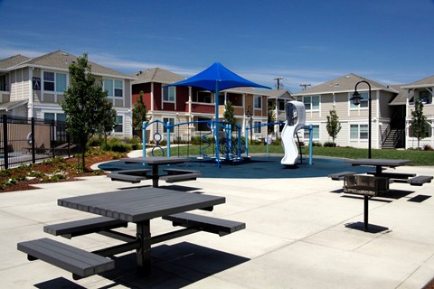 an outdoor playground with picnic tables in front of apartment buildings