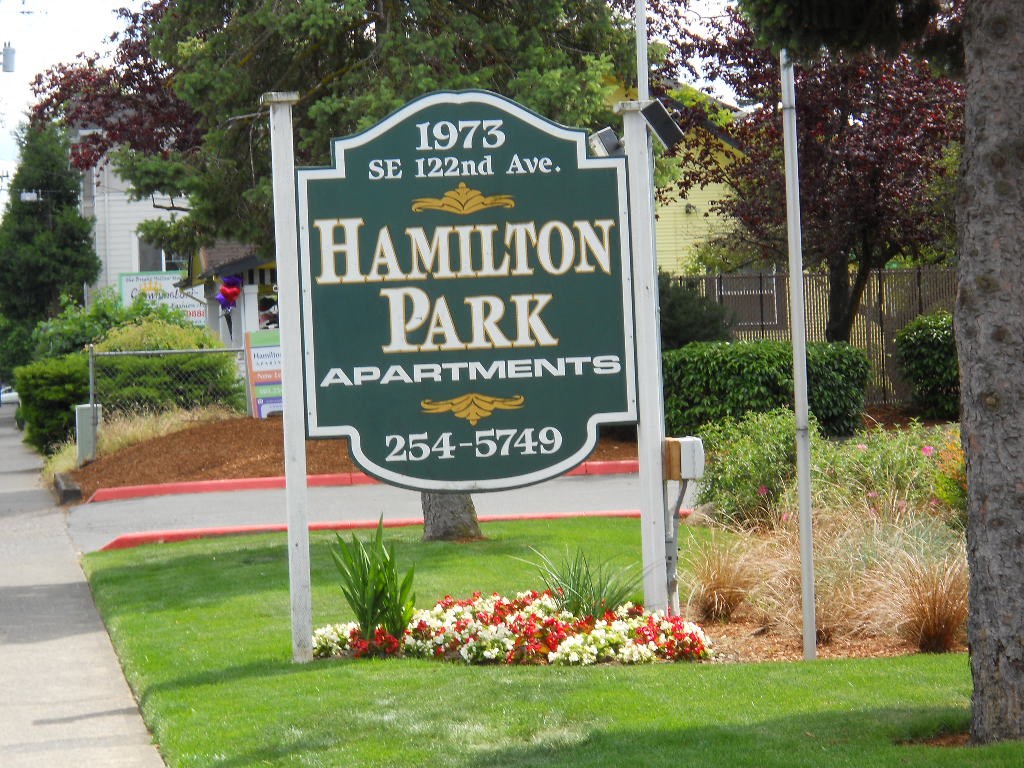 a sign apartments in front of a lawn and flowers
