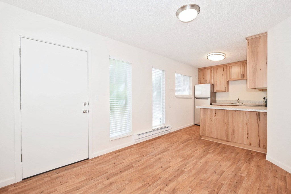 an empty living room and kitchen with wood floors and white walls