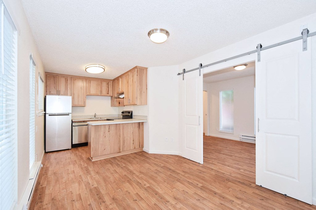 an empty kitchen with white appliances and wood flooring