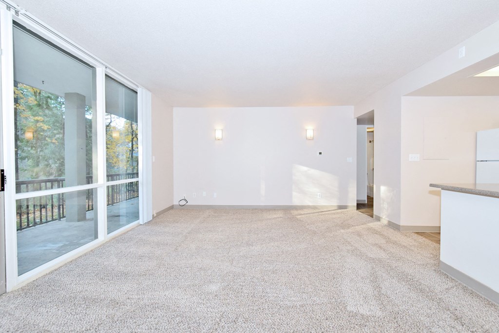 the living room and kitchen of an apartment with white walls and carpet