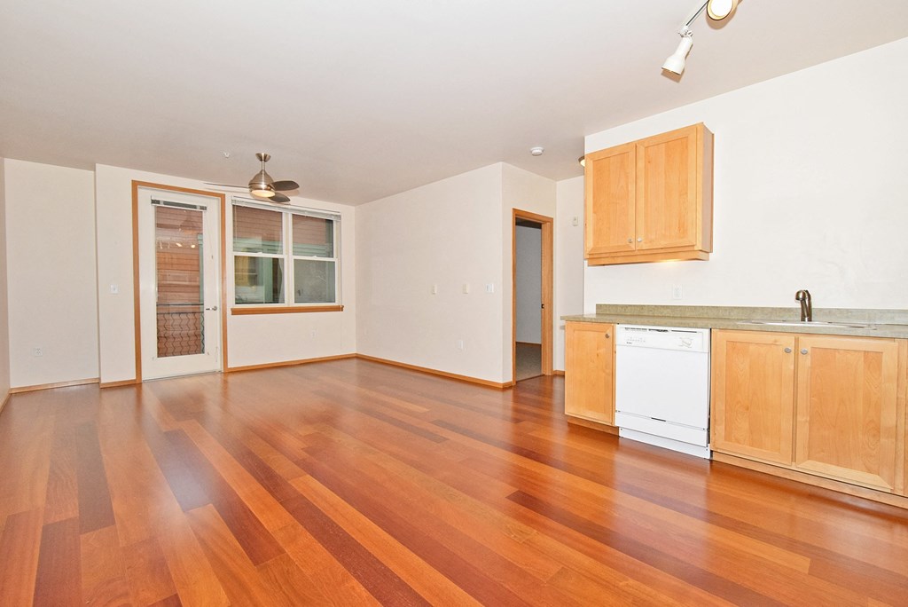 an empty kitchen and living room with wood floors and white appliances