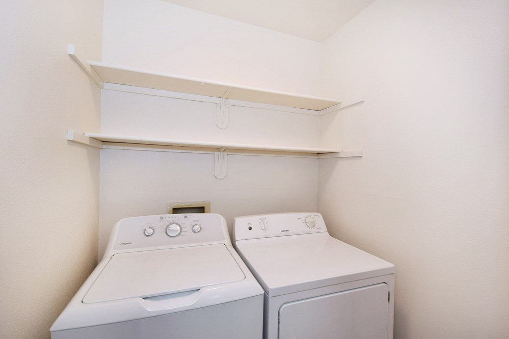 a white washer and dryer in a white room with a shelf above it
