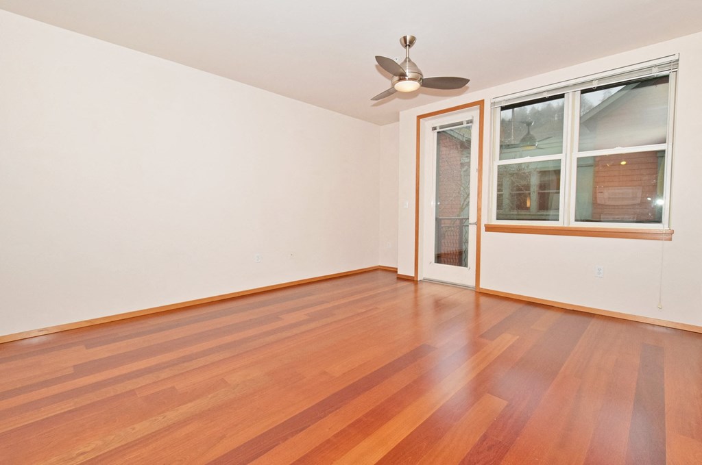 an empty living room with wood floors and a window and a ceiling fan