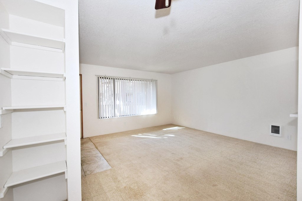 an empty living room with a window and white shelves