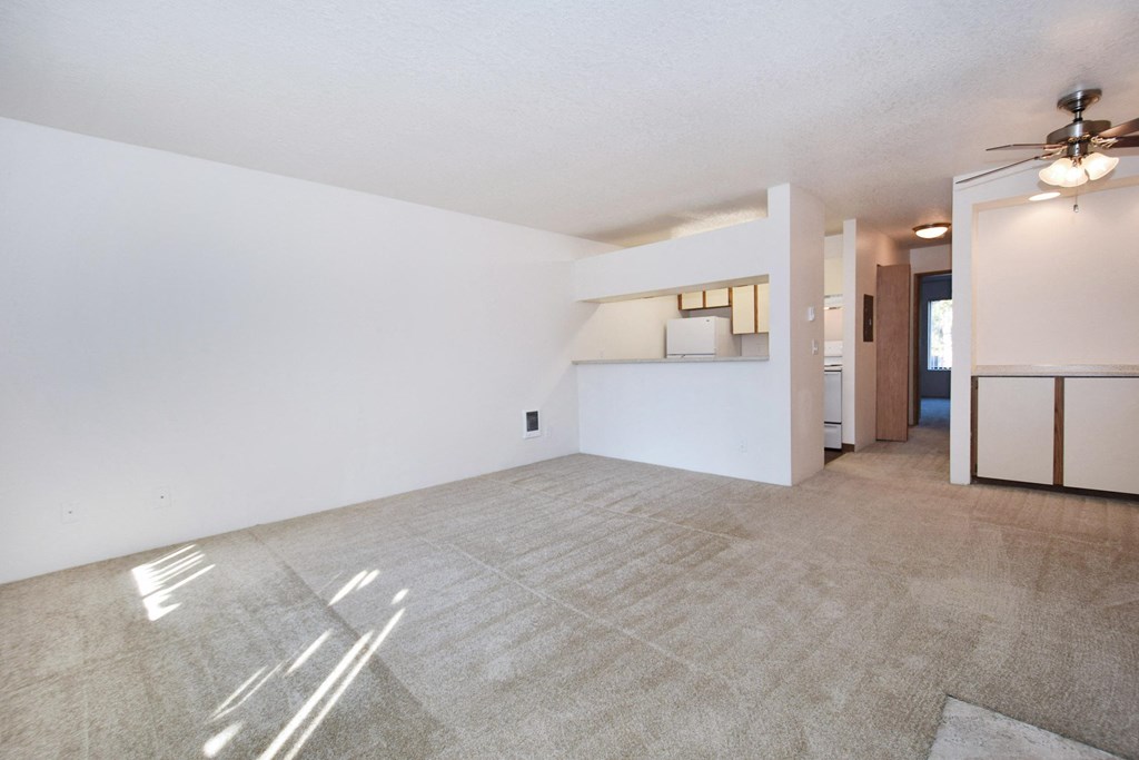 an empty living room with a ceiling fan and a kitchen
