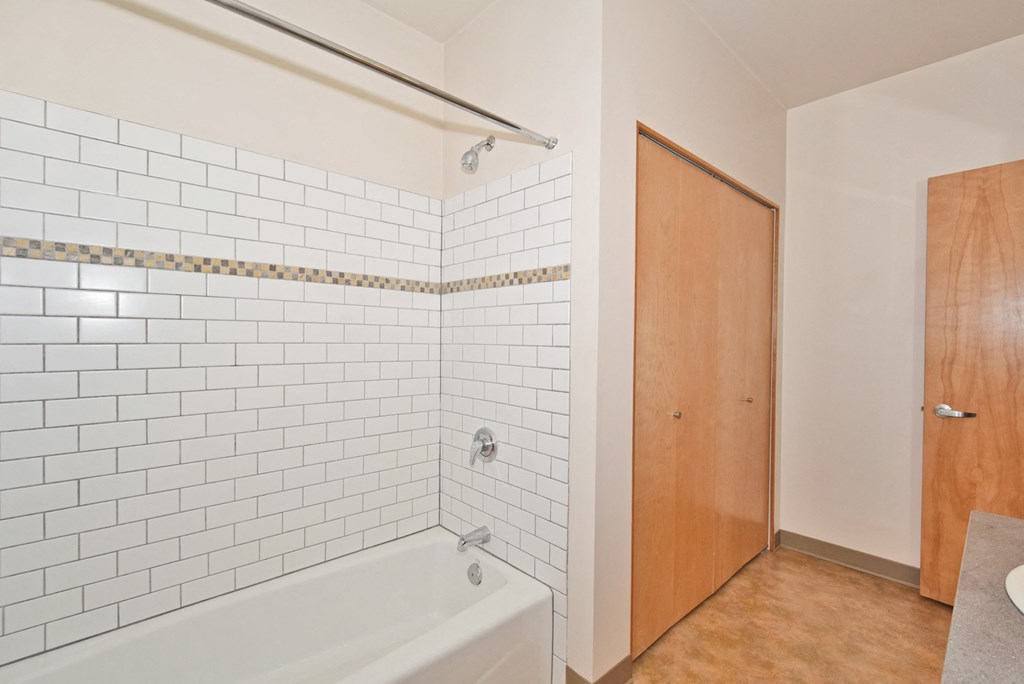 a white tiled bathroom with a tub and a wooden door