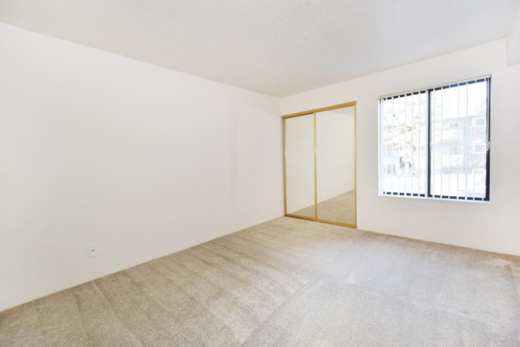 the spacious living room of an apartment with a large window and white walls