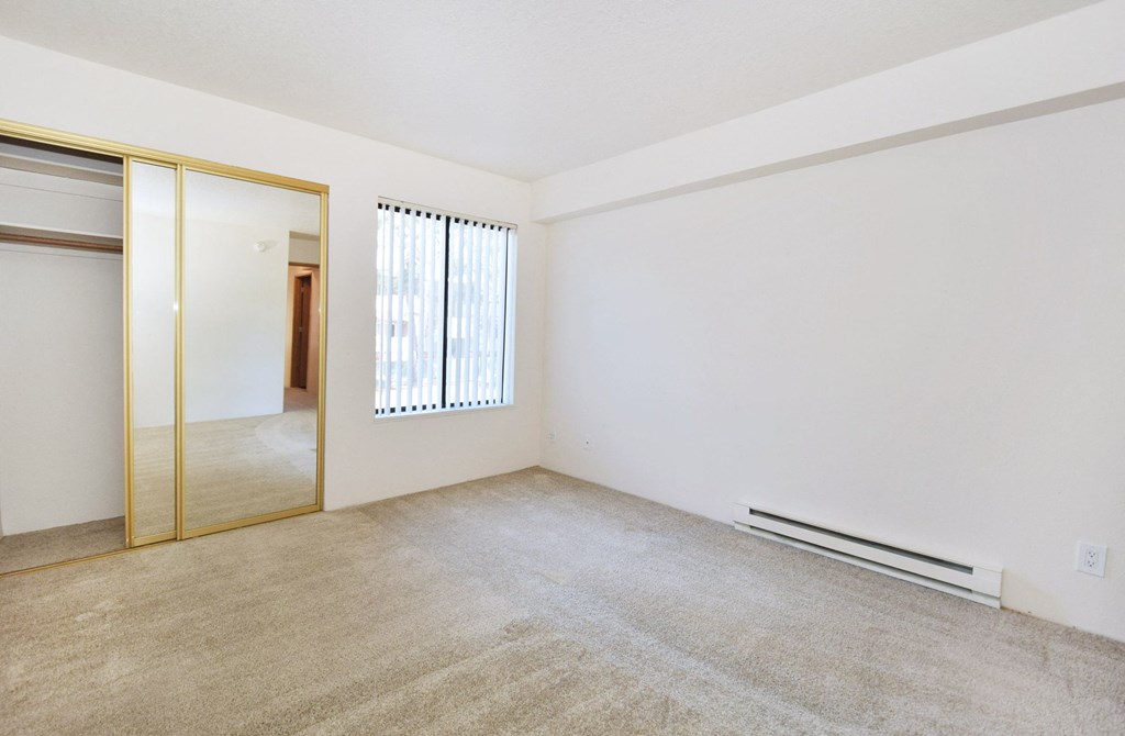 an empty living room with white walls and a mirror in the corner