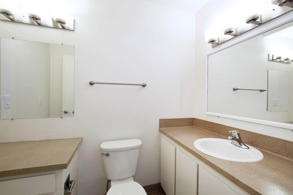 A white toilet sits in a bathroom with a sink and mirror.