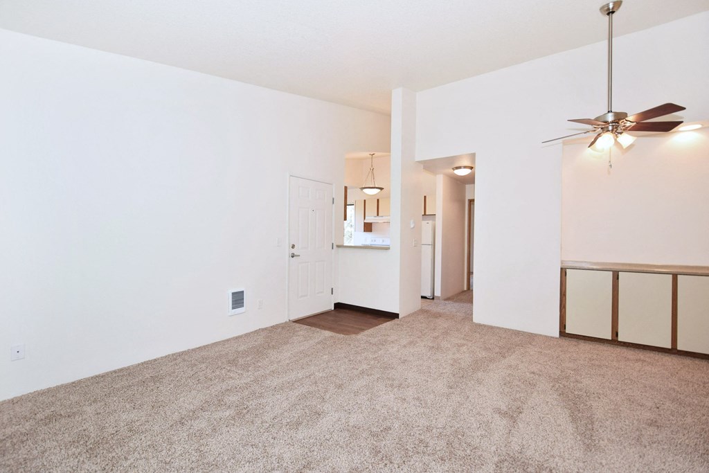 the living room and dining room of an apartment with carpet and a ceiling fan