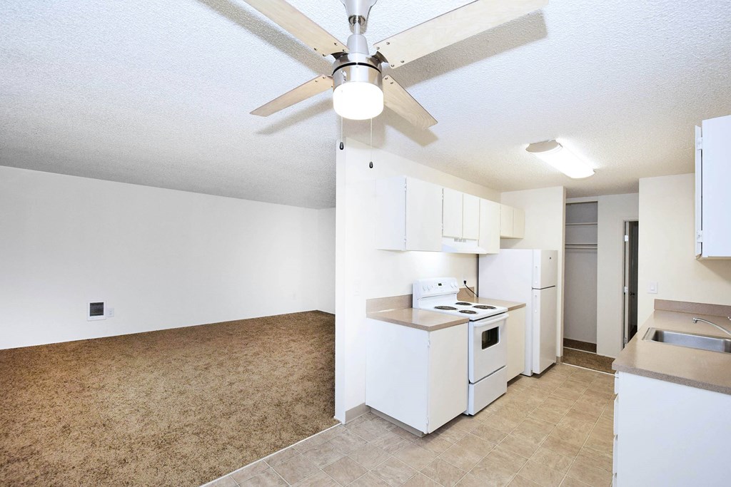 A kitchen with white appliances and a ceiling fan.