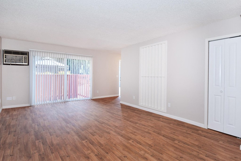 the spacious living room of an apartment with wood flooring and white walls