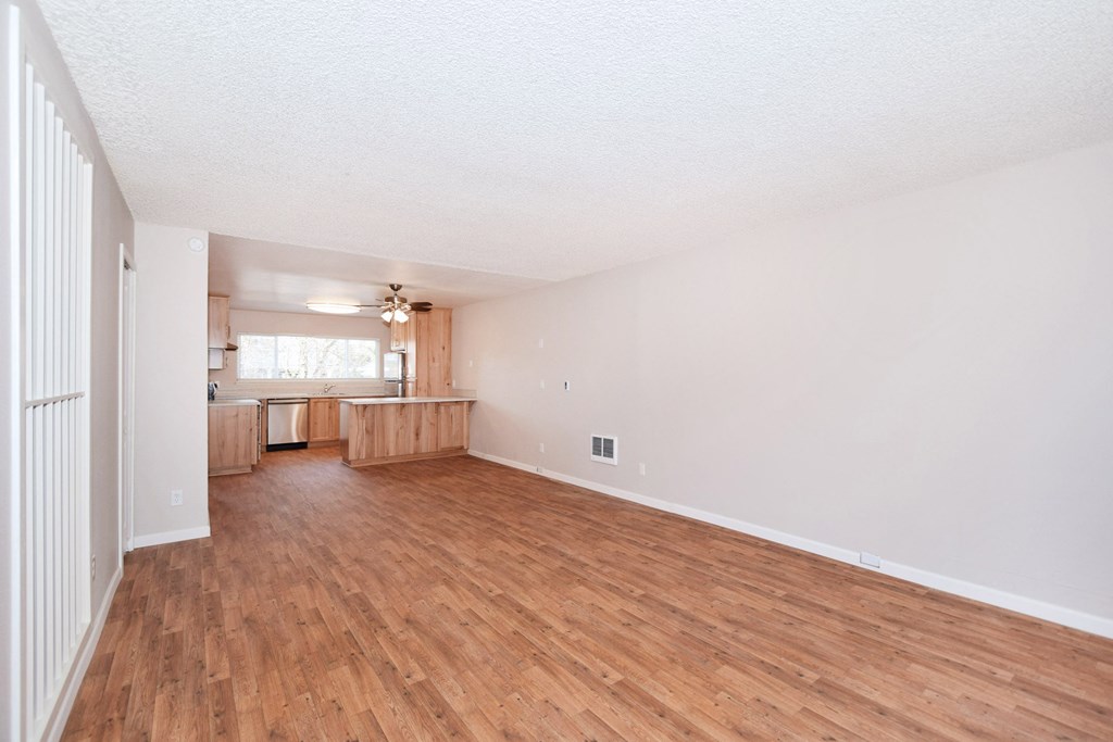an empty living room with wood flooring and a kitchen