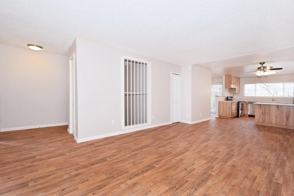 an empty living room with wood flooring and a kitchen