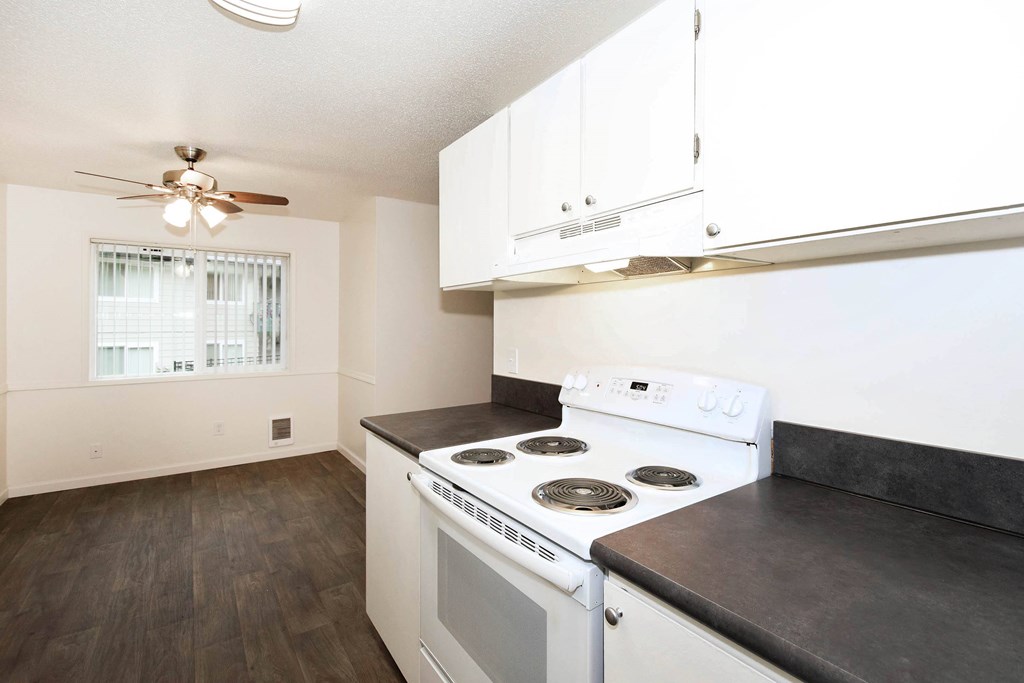 A white stove in a kitchen with white cabinets and a ceiling fan.