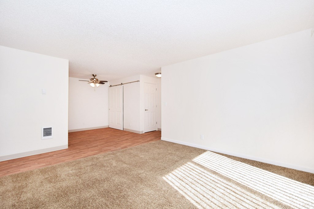 a spacious living room with white walls and wood flooring and a ceiling fan