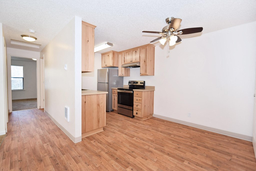 an empty living room and kitchen with wood flooring and a ceiling fan