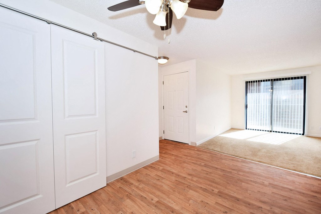 the living room and dining room of an apartment with white walls and wood flooring