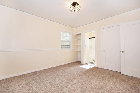 a bedroom with white walls and carpet and a door to a closet