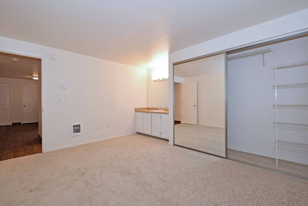 an empty living room with a mirror and a kitchen