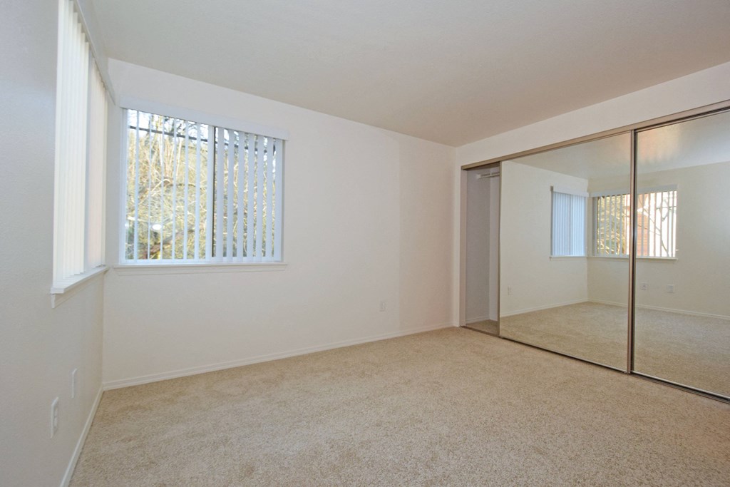 an empty living room with a large window and a mirrored closet