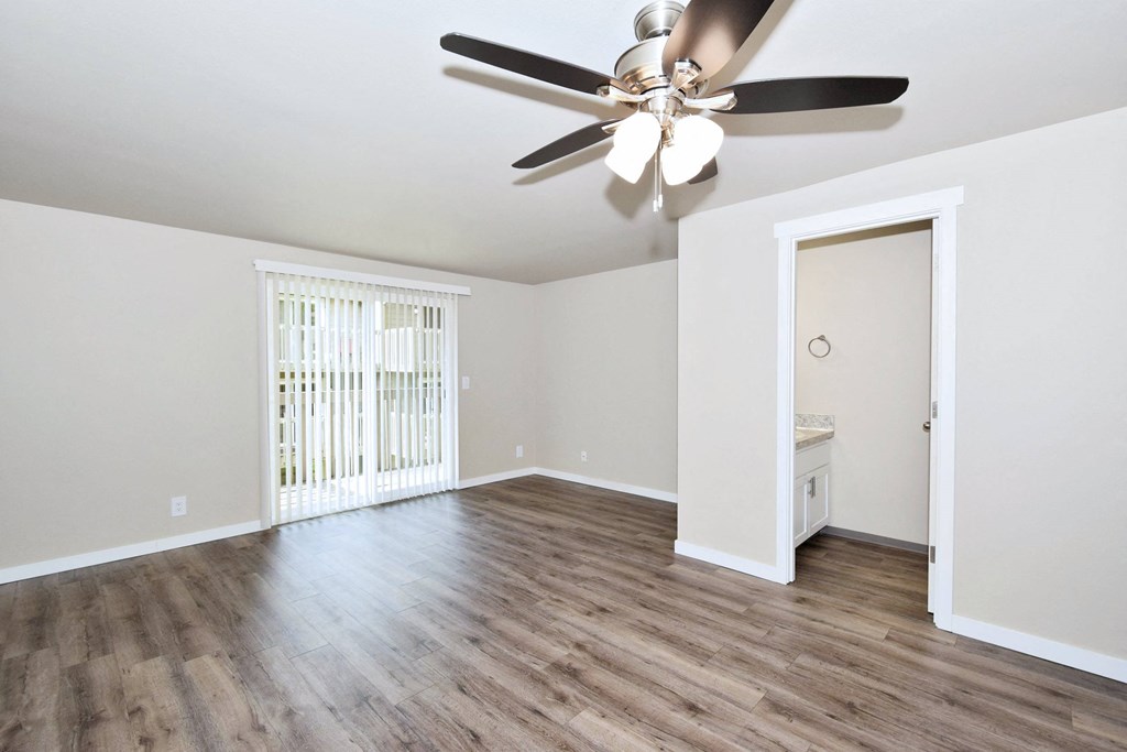 an empty living room with a ceiling fan and a door to a bathroom