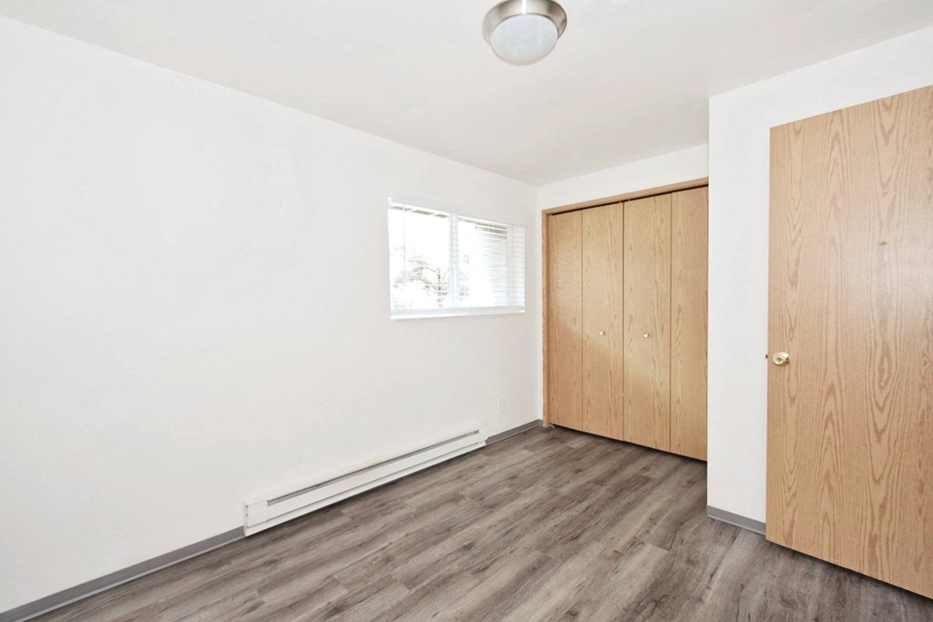 an empty room with white walls and wood flooring and a wooden closet