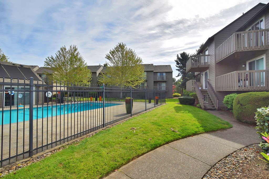 the view of a swimming pool in front of an apartment building with a fence