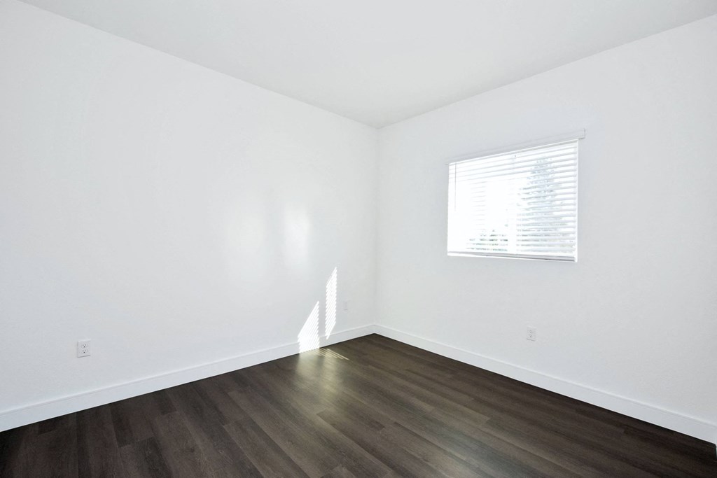 a bedroom with white walls and wood floors and a window
