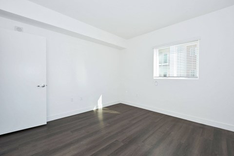a bedroom with white walls and wood floors and a window