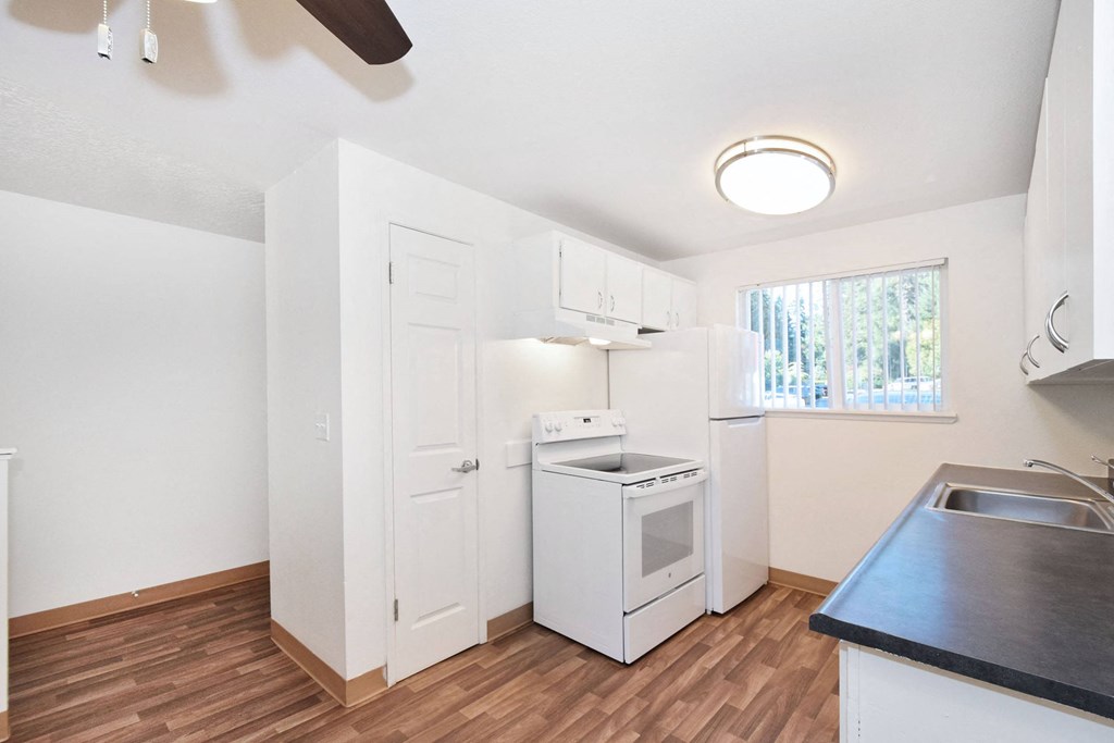 an empty kitchen with white appliances and a window