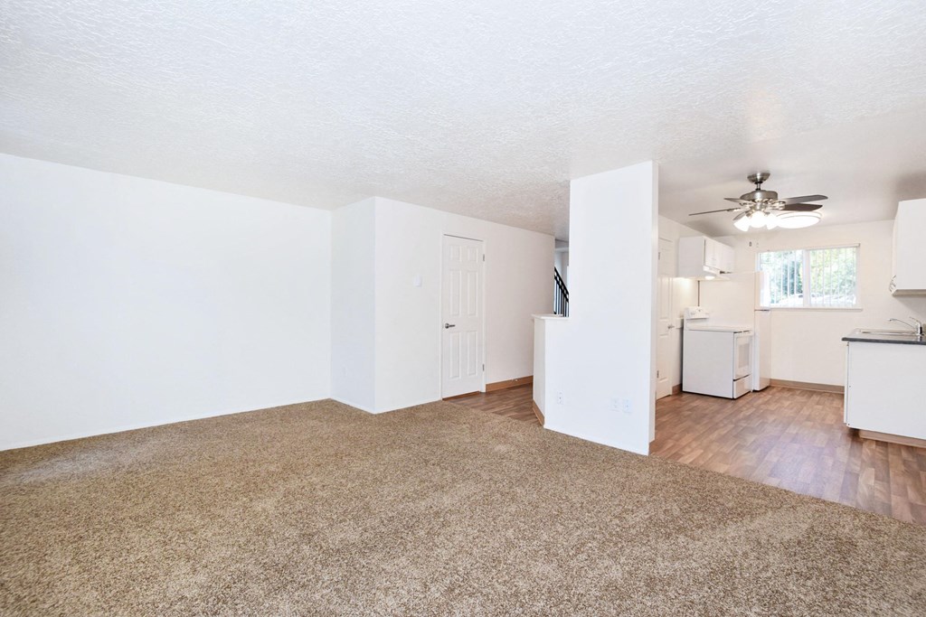 an empty living room with a kitchen and a ceiling fan