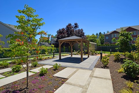 A gazebo is surrounded by a garden with a paved walkway.