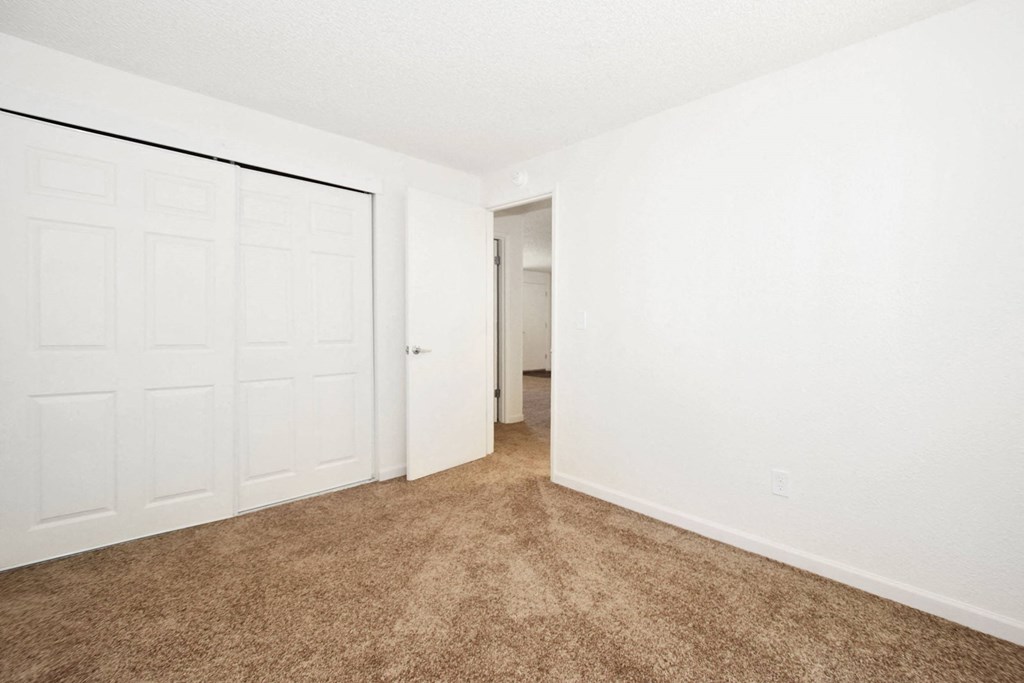 an empty bedroom with a closet and a door to a hallway