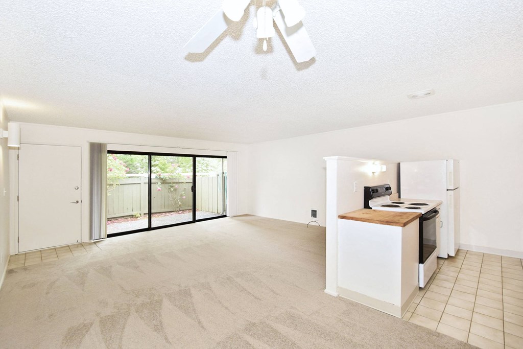 an empty living room with a kitchen and a sliding glass door