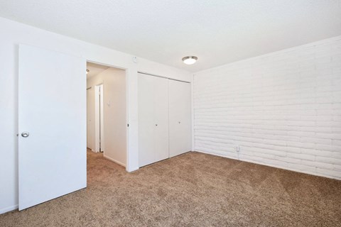 a bedroom with white walls and carpet and a door to a closet
