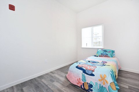 a bedroom with white walls and a bed with a colorful bedspread and a window