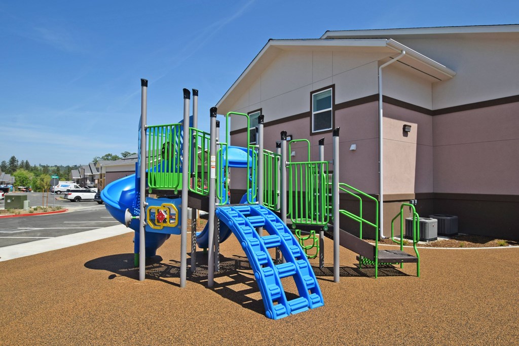 A playground with a blue slide and green railings.