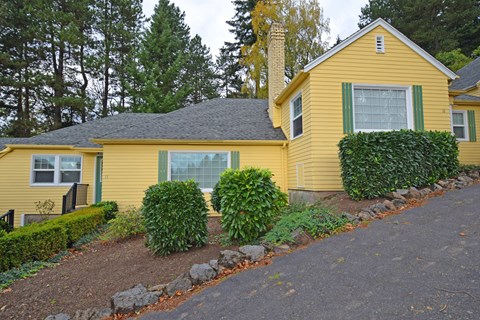 a yellow house with green shutters and a gravel driveway
